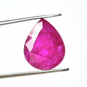 May include: A faceted, pear-shaped ruby gemstone, held by tweezers against a white background. The ruby displays a vibrant, deep pink color with multiple facets reflecting light. The gemstone's shape is a teardrop, with a pointed end.