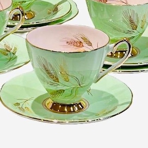May include: A collection of vintage teacups and saucers. The teacups are light green with gold detailing and a wheat motif. The interior of the cups is pink. The saucers are light green with gold trim and a wheat design.