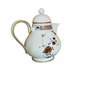 Może przedstawiać: Biały porcelanowy imbryk ze złotym uchwytem i wykończeniem. Imbryk zdobiony wzorami kwiatowymi w odcieniach czerwieni, niebieskiego i żółtego. Ozdobny pas z geometrycznym wzorem otacza górną część.