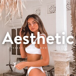 May include: A woman in a white bikini top and white bikini bottoms poses in front of a white wall with the word "Aesthetic" in large white letters. The text "@presetdesign mobile preset" is below the word "Aesthetic".