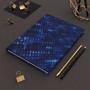 May include: A closed journal with a blue binary code design. The notebook is surrounded by gold binder clips, pencils, and a decorative gold object. The cover features a pattern of blue dots and numbers.