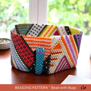 May include: A colorful beaded bracelet with a geometric pattern. The bracelet is made with black, white, red, orange, yellow, purple, and turquoise beads. The bracelet has a clasp made of turquoise and purple beads.