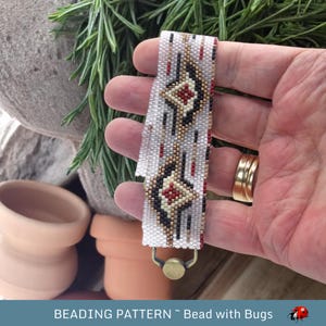 May include: White beaded bracelet with a geometric pattern in black, red, and gold. The bracelet has a clasp closure.