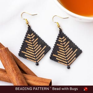 May include: A pair of black and gold beaded earrings with a geometric design. The earrings are shaped like a diamond and have a gold bead at the bottom. The earrings are hanging from gold hooks.