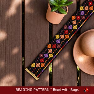 May include: A beaded pattern on a black background with colorful floral designs in red, orange, yellow, and purple. The pattern is displayed on a wooden surface with a small potted plant and a copper-colored dish. The text "BEADING PATTERN ~ Bead with Bugs" is at the bottom.