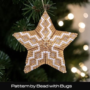 May include: A five-pointed star ornament crafted from small metallic gold and opaque white beads arranged in a geometric diamond pattern. The star features a hanging loop at the top and displays the text Pattern by Bead with Bugs below.