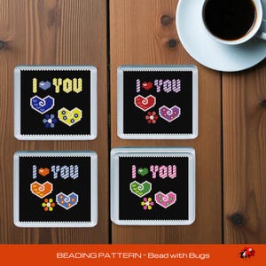 May include: Four square coasters with a black background and the words "I ♥ YOU" in a pixelated font. Each coaster features a different color scheme of hearts and flowers. The coasters are on a wooden surface, with a cup of coffee in the background.