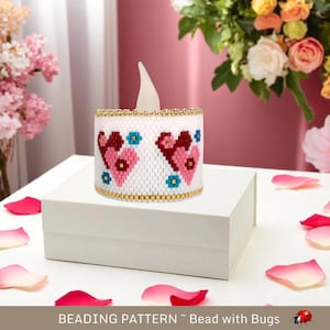 Puede incluir: Un portavelas blanco de cuentas con un diseño de corazón rosa y rojo. El portavelas está sobre una caja blanca con un fondo blanco.