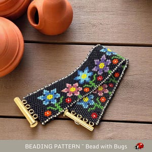 Könnte beinhalten: Ein schwarzes Perlenarmband mit einem Blumenmuster. Das Armband zeigt bunte Blumen, grüne Blätter und rote Käfer. Das Armband hat goldene Metallverschlüsse.