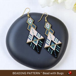 May include: A pair of geometric beaded earrings with a black, white, blue, and gold color scheme. The earrings are diamond-shaped and dangle from gold hooks.