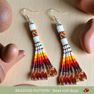 May include: A pair of beaded earrings with a white base and colorful geometric patterns. The earrings have a long, dangling design with multiple strands of beads in shades of orange, red, brown, and white. The earrings are finished with a gold hook.
