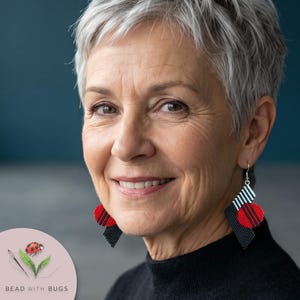 May include: Geometric dangle earrings featuring a diamond-shaped black beaded base with a red circular accent and white striped detailing. The earrings hang from silver-toned metal hooks and display a bold, contrasting color palette.
