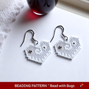 May include: A pair of white heart-shaped earrings with silver beads. The earrings are made with a beading technique and have a delicate, intricate design.