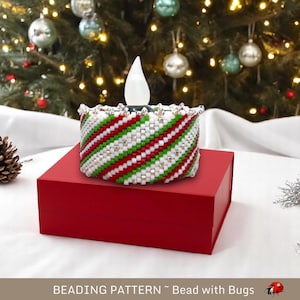 May include: A red, white, and green beaded candle holder with a white light inside. The candle holder is sitting on a red box. The text "BEADING PATTERN - Bead with Bugs" is at the bottom of the image.
