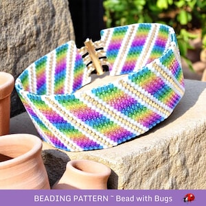 Puede incluir: Un brazalete de cuentas de colores arcoíris con fondo blanco y detalles dorados. El brazalete está hecho con pequeñas cuentas de semillas y está diseñado en un patrón diagonal.