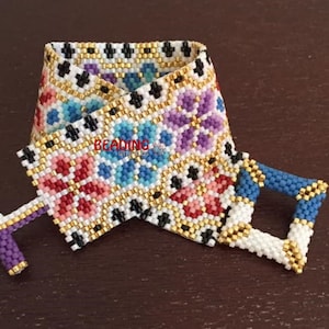 May include: A white beaded bracelet with a colorful floral pattern and gold accents. The bracelet has a clasp closure.