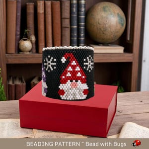 May include: A beaded bracelet pattern featuring a snowman with a red hat and black and white snowflakes. The pattern is called "Bead with Bugs".