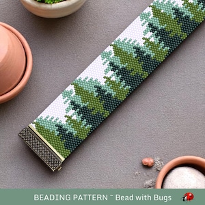 May include: A beaded bracelet featuring a pattern of green and white trees. The bracelet has a gold clasp and is on a grey surface.