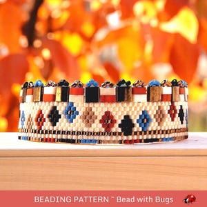 Op de afbeelding: Een kralenarmband met een geometrisch patroon in crème, rood, zwart, blauw en bruin. De bovenste rij heeft afwisselende kleuren en vormen. De tekst onderaan luidt "BEADING PATTERN ~ Bead with Bugs."