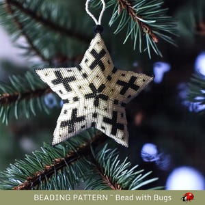 May include: A white and black beaded star ornament hanging on a green Christmas tree. The star is made of small beads and has a geometric pattern.