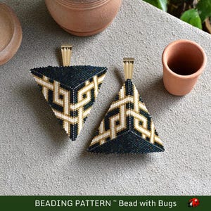 Może przedstawiać: Dwa trójkątne, koralikowe zawieszki w kolorze czarnym i złotym z geometrycznym wzorem. Zawieszki mają złote kółka do zawieszenia na łańcuszku lub sznurku. Na dole zdjęcia widnieje napis "Beading Pattern - Bead with Bugs".