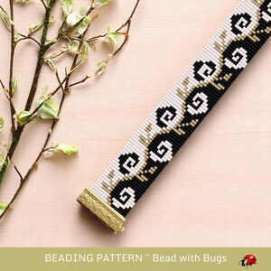 May include: A beaded bracelet featuring a repeating pattern of black and white swirls and floral designs. The bracelet has a gold-coloured clasp and is set against a light pink background. The text "BEADING PATTERN ~ Bead with Bugs" is at the bottom.