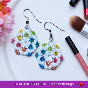 Peut inclure: Une paire de boucles d'oreilles en perles colorées sur fond blanc. Les boucles d'oreilles ont la forme d'une fleur avec un motif circulaire au centre. Les perles sont dans des tons de bleu, vert, jaune, rose et orange.