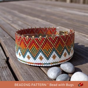 Puede incluir: Un brazalete de cuentas con un patrón geométrico en tonos de rojo, naranja, verde, blanco y dorado. El brazalete está hecho con pequeñas cuentas de semillas y tiene un diseño de chevron.