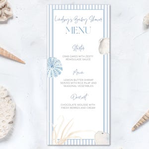 May include: A blue and white striped menu card for a baby shower with the text "Lindsey's Baby Shower Menu" at the top. The menu includes a starter, main course, and dessert. The menu is decorated with blue and white seashells and seaweed.