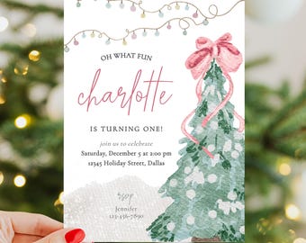 May include: A birthday invitation card featuring a watercolor Christmas tree with a pink bow, string lights, and text reading: OH WHAT FUN, charlotte IS TURNING ONE!, join us to celebrate, Saturday, December 5 at 2:00 pm, 12345 Holiday Street, Dallas, RSVP Jennifer 123-456-7890.