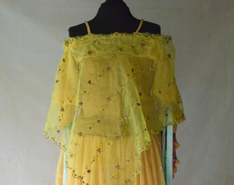 May include: A yellow off-the-shoulder dress with a sheer overlay and floral embroidery. The dress has a flowing skirt and is decorated with sequins.
