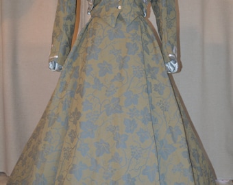 May include: A long, flowing, green and blue dress with a white geometric pattern around the hem. The dress has a matching jacket with a white geometric pattern around the neckline.
