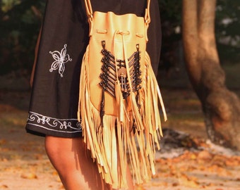 May include: A tan leather bucket bag with fringe and black bead accents. The bag has a long strap and is worn over the shoulder.