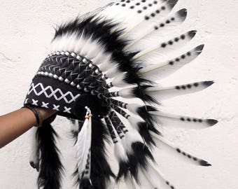 Puede incluir: Tocado de plumas blanco y negro con ribete blanco y negro. El tocado se lleva en la cabeza de una persona.