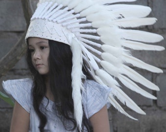 Puede incluir: Una persona joven con un tocado de plumas blancas. El tocado está hecho de plumas blancas y tiene una banda de cuero blanco alrededor de la base.