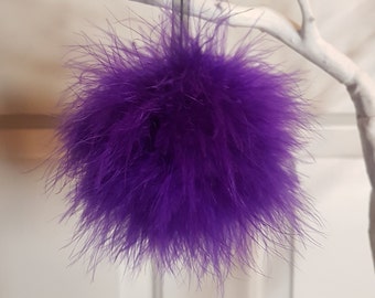 May include: Purple feather pom pom ornament hanging from a white branch.
