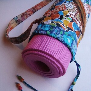 May include: A pink yoga mat rolled up and secured in a colorful fabric carrying case with a long strap. The case has a floral pattern with blue, orange, and brown accents.