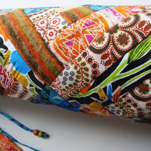 May include: A colorful patchwork yoga mat with a blue and orange drawstring closure. The mat is made of different fabrics with floral and geometric patterns.