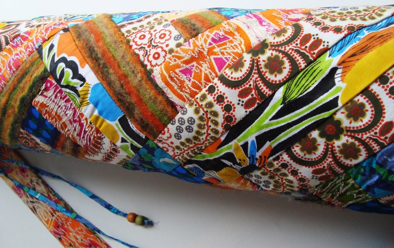 May include: A colorful patchwork yoga mat with a blue and orange drawstring closure. The mat is made of different fabrics with floral and geometric patterns.