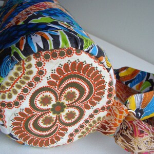 May include: A colorful fabric bag with a round bottom and a floral pattern. The bag has a long strap and a drawstring closure.