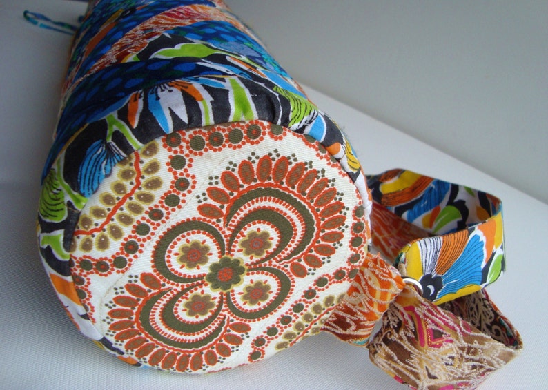 May include: A colorful fabric bag with a round bottom and a floral pattern. The bag has a long strap and a drawstring closure.