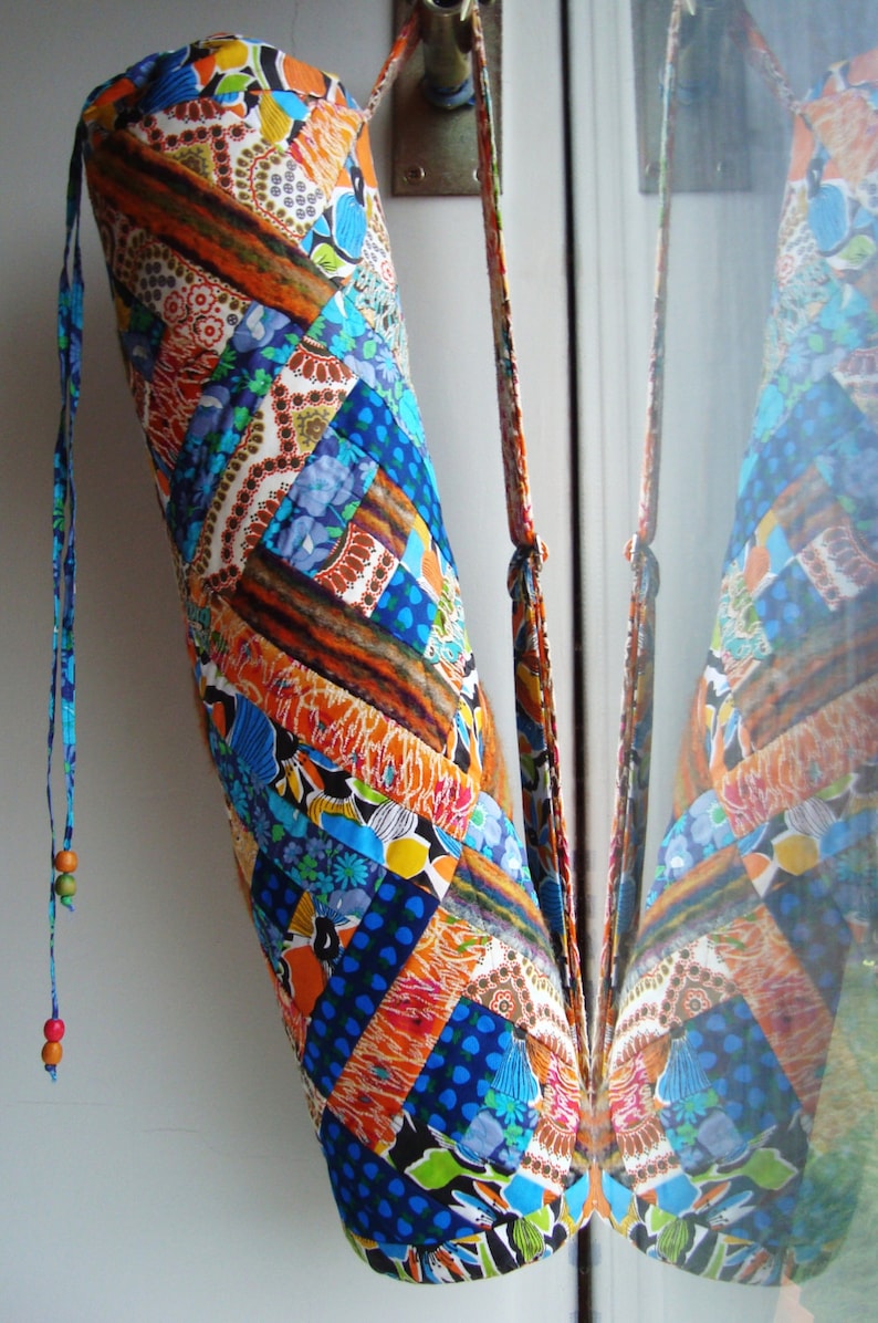 May include: A colorful yoga mat bag with a patchwork design in shades of blue, orange, and brown. The bag has a long strap and a drawstring closure.