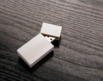 Puede incluir: Una memoria USB de madera blanca con una tapa deslizante. La unidad está abierta y el conector USB es visible.