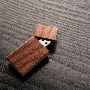 Puede incluir: Una memoria USB de madera con una tapa deslizante. La memoria está hecha de madera marrón oscura y tiene un conector USB plateado.
