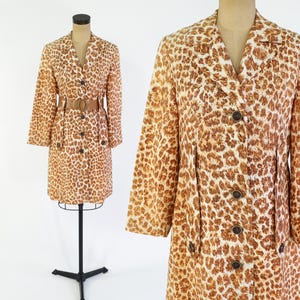 Op de afbeelding: Een vintage jas met luipaardprint met een reverskraag, lange mouwen en een knoopsluiting. De jas heeft een bijpassende riem en wordt op een mannequin getoond. Het patroon van de jas is bruin en beige.
