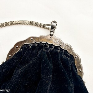 May include: A black velvet purse with a silver metal frame and chain. The frame has a decorative design and the initials "H.W." are engraved on the front.