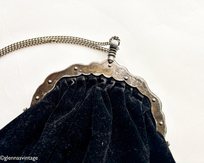May include: A black velvet purse with a silver metal frame and chain. The frame has a decorative design and the initials "H.W." are engraved on the front.