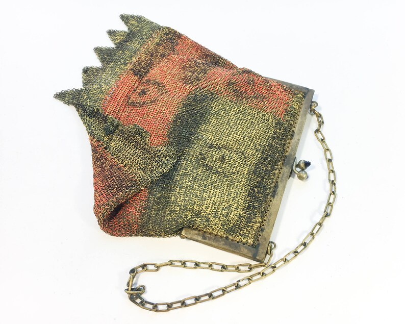 K&ouml;nnte beinhalten: Eine Vintage-Mesh-Handtasche mit einer Kettenkette. Die Tasche ist aus feinem Mesh-Material gefertigt und hat ein geometrisches Muster in Gr&uuml;n-, Schwarz- und Rott&ouml;nen. Die Tasche hat einen Metallverschluss und eine Kettenkette.