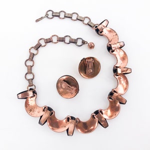 May include: A copper necklace with a chain and a matching pair of earrings. The necklace is made of a series of crescent-shaped copper pieces with black accents.
