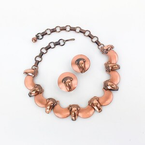 May include: A copper necklace and earrings set with a chain and a series of crescent-shaped pendants with a raised design.